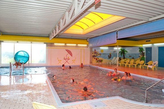 Een binnenzwembad met kinderen die spelen, kleurrijke muren en een zonnige inrichting.